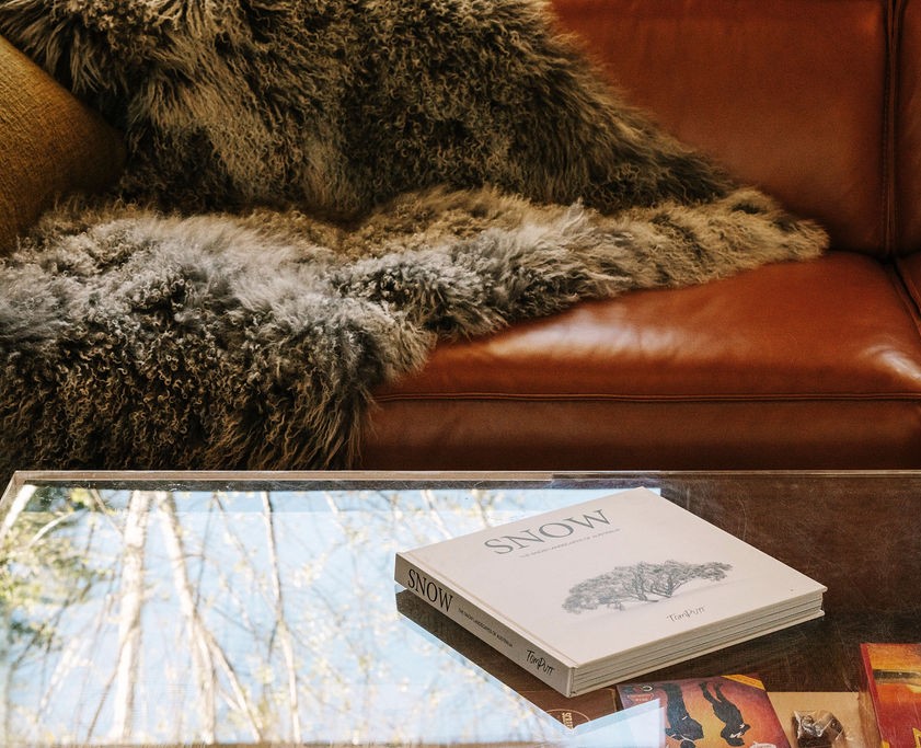 Cozy mid-century living room with a leather sofa draped in a fur throw and a coffee table topped with books at Bomen Harrietville; Accommodation Bright, Mid Century Stays, Victoria Alpine