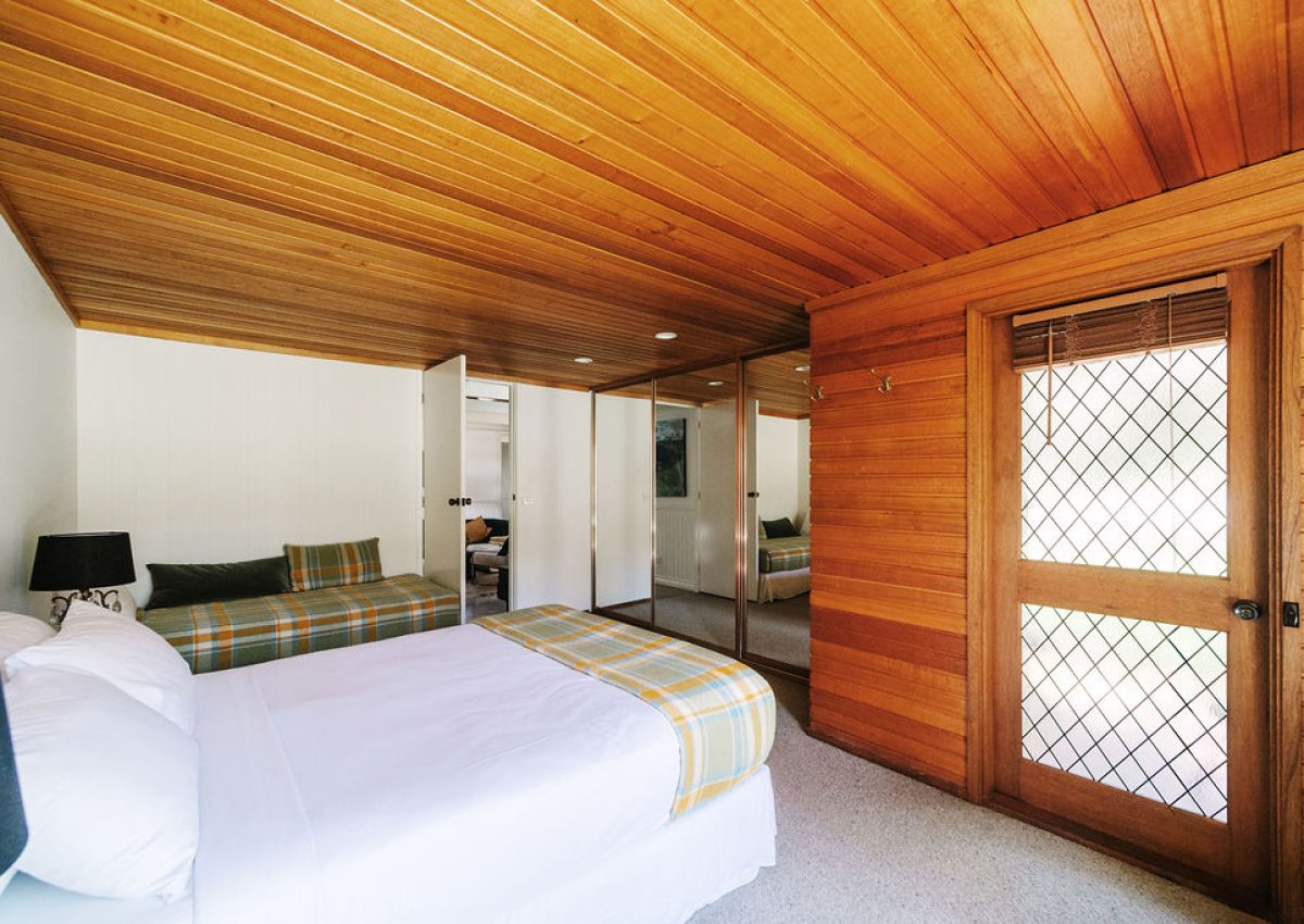 Spacious master bedroom at Blackwood Lodge featuring a queen bed and single bed with plaid bedding, wood-panelled ceiling and walls, and access to a private patio through a lattice door; Accommodation Bright, Mid Century Stays, Victoria Alpine