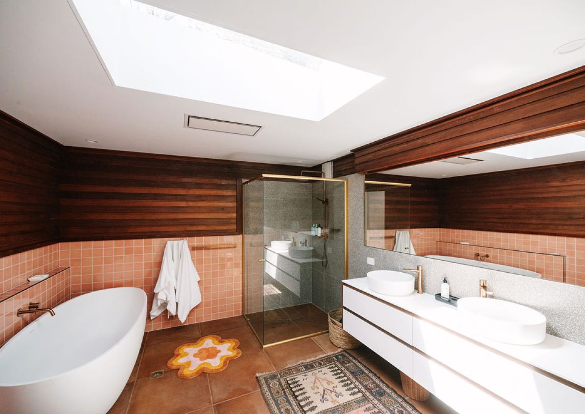 Wide-angle view of a luxurious ensuite bathroom at Bomen Harrietville featuring a freestanding bathtub, glass-enclosed shower, double vanity with vessel sinks, warm timber accents and skylight; Accommodation Bright, Mid Century Stays, Victoria Alpine