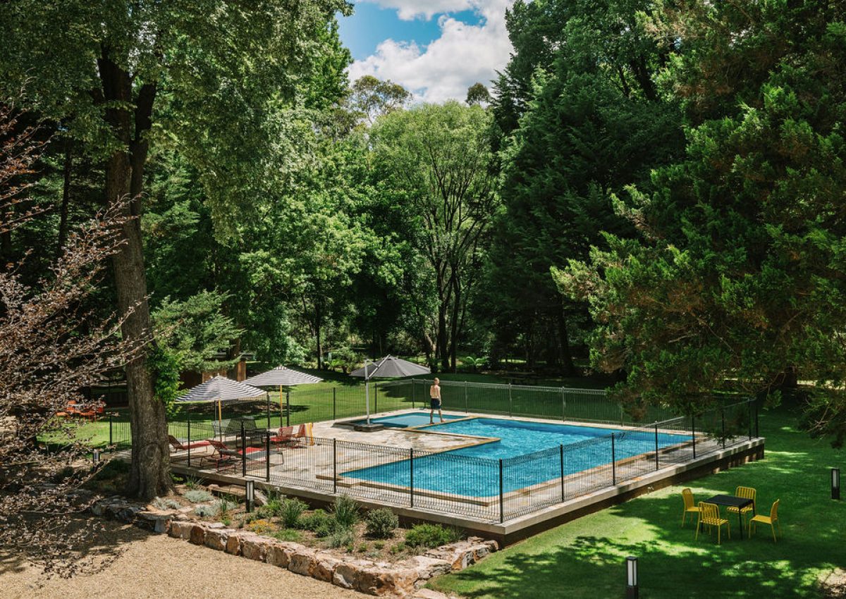 Outdoor leisure area at Bomen Harrietville with a fenced rectangular swimming pool, colourful umbrellas, seating, and lush trees in the Victoria Alpine region; Accommodation Bright, Mid Century Stays, Victoria Alpine